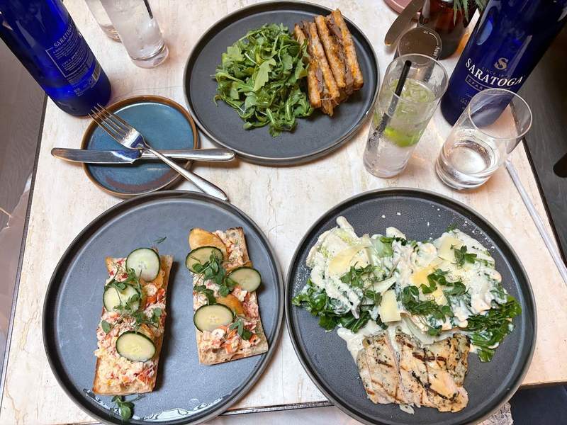 A date night dinner at Parker's. On the table is lobster toast with cucumbers and chips, Caesar salad, and chopped cheese sandwich plated on a table.