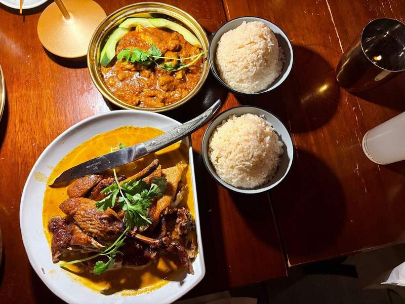 A dinner date with dishes of Curry Duck and Squid Rendang with cups of jasmine rice on a wooden table at Laut in Union Square.