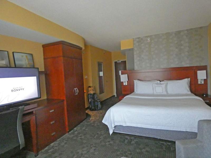 A hotel bedroom with a bed, dresser, clothes cabinet and TV showing.