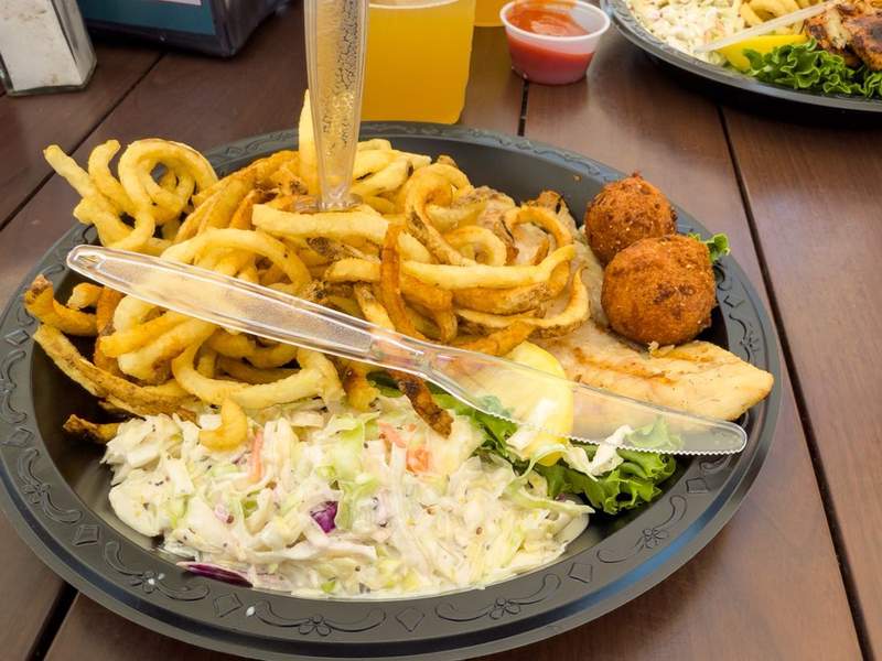 Grilled sheepshead fish platter with curly fries, coleslaw, and two hushpuppies on a dockside table overlooking Silver Lake, Ocracoke