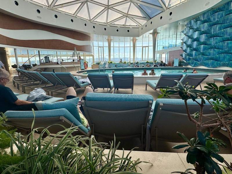 Indoor swimming pool with floor to ceiling windows and ocean blue cushioned lounge chairs