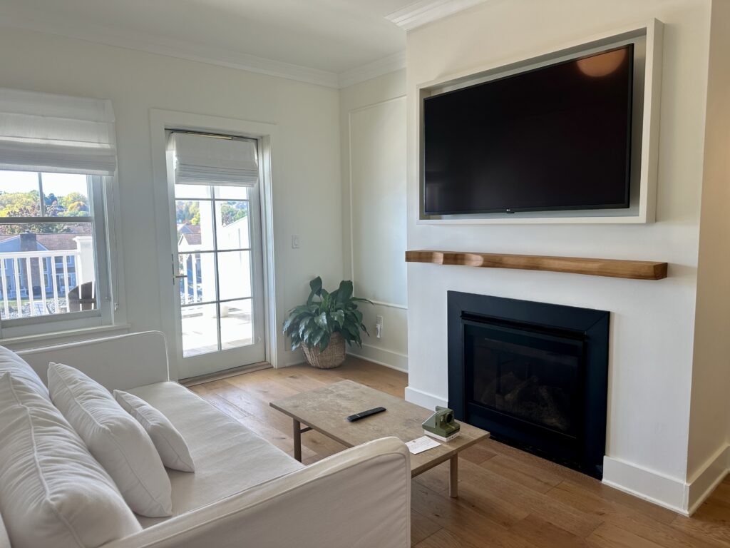 Parlor with deep white couch, fireplace and tv with door to outside deck at the Lake House on Canandaigua in NY's Finger Lakes.