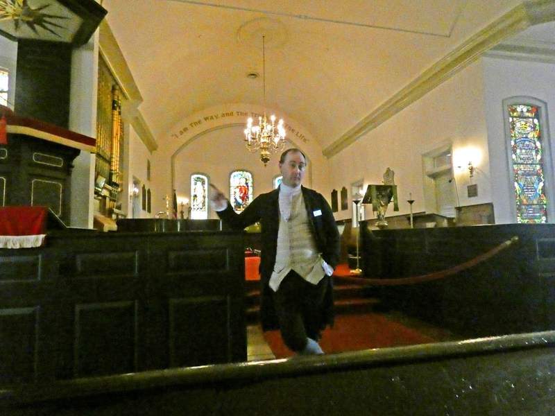 Man in colonial dress standing i front of altar in a church.