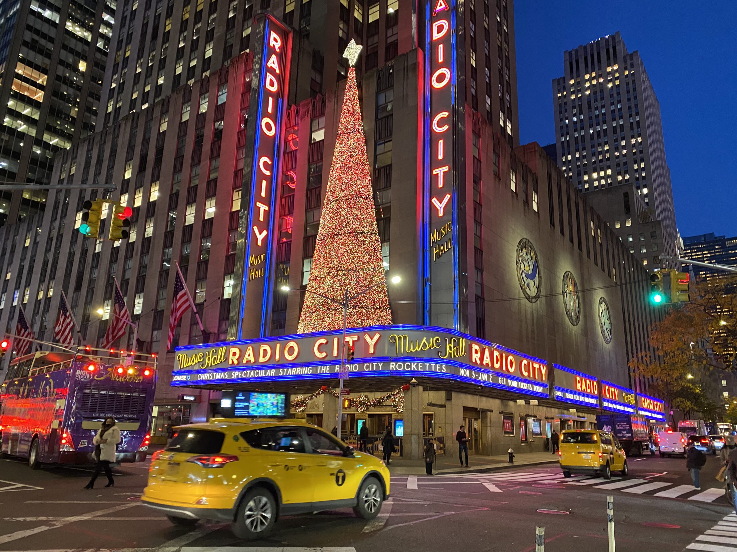 Radio City Music Hall with large tree and taxi in foreground during Christmas in NYC