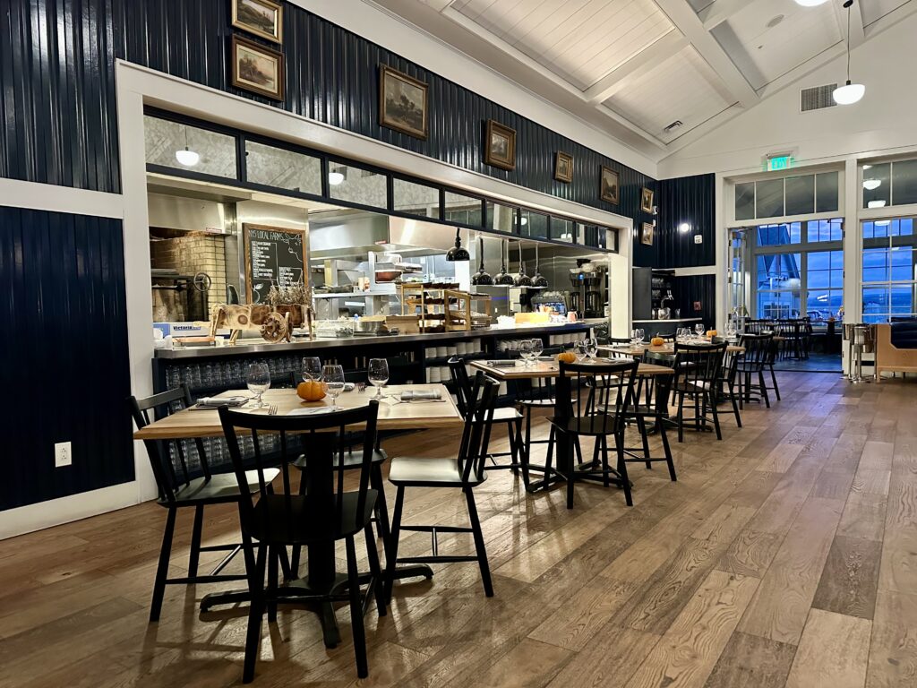 Open kitchen with tables and black dining chairs in the Rose Tavern, the fine dining restaurant at the Lake House on Canandaigua.