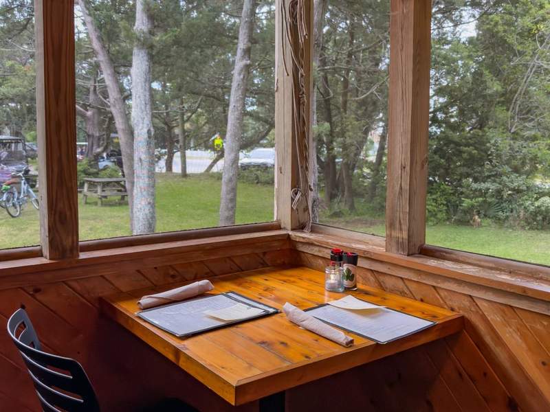 Screened porch dinner table at dusk with warm light and a faint firefly glow in the yard, Ocracoke Island, North Carolina.