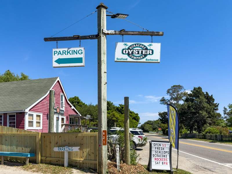Street view of the Ocracoke Oyster Company sign on Ocracoke Island, blue sky and island shops nearby.