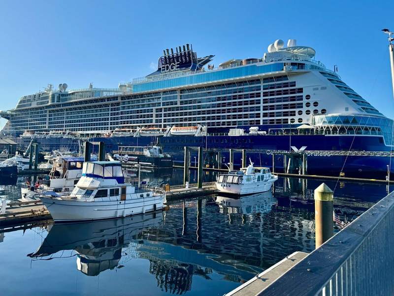 The Celebrity Edge a blue and white ship docked in Ketchikan. A marina is in front of the ship with fishing and tour boats.