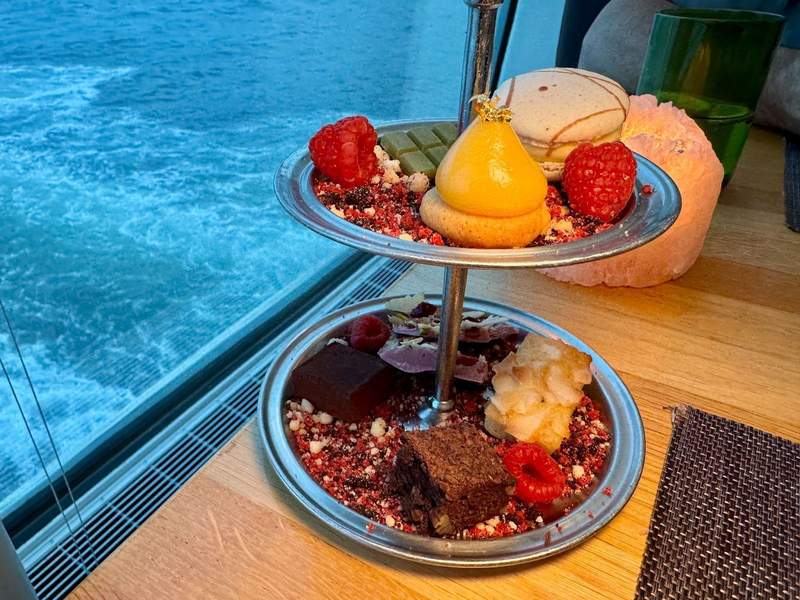 Tiered tray with yummy treats including brownies, candy, macarons, and raspberries on a bed of sprinkles.