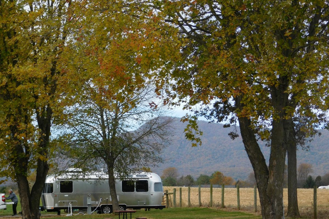 An rv sitting at a campground surrounded by fall leaves and mountains.