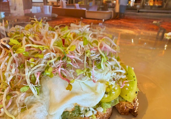 Avocado toast topped with heirloom tomatoes, egg, crumbled cheese, and colorful microgreens at Proof restaurant in Four Seasons Scottsdale