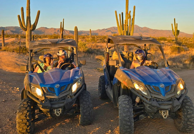 Two blue dune buggies on a desert trail at sunset with passengers and saguaro cacti in the background near Scottsdale