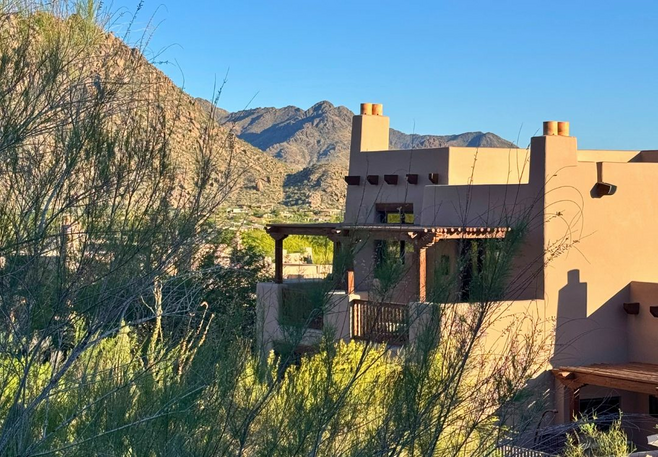 Adobe-style casita with mountain backdrop surrounded by desert brush under a clear blue sky