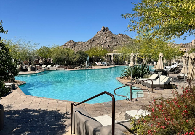 Resort pool surrounded by loungers, desert plants, and mountain views under a clear blue sky