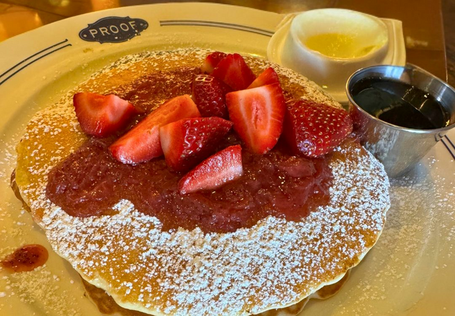 Stack of strawberry pancakes topped with fresh berries, syrup, and powdered sugar at Proof restaurant in Four Seasons Scottsdale