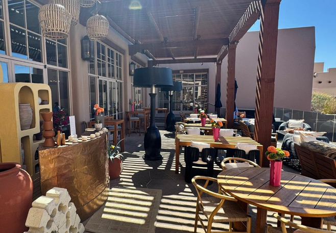 Shaded outdoor dining patio at Onyx Bar & Lounge with wooden tables, colorful flower arrangements, and lounge seating at Four Seasons Scottsdale