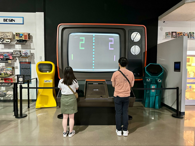 Man and woman playing a giant Atari Pong console at the National Videogame Museum, a must-visit on a Frisco Texas sports getaway.