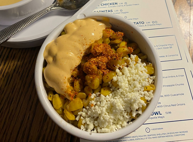 a bowl of roasted yellow corn covered in cojito cheese, tajin and cheese sauce.