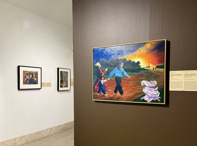 Three paintings displayed on the walls of the Art Museum of South Texas. Each painting has a descriptive sign next to it explaining the piece in both English and Spanish. The painting in the foreground shows a man and boy walking with a Day of the Dead dressed skeleton behind them.