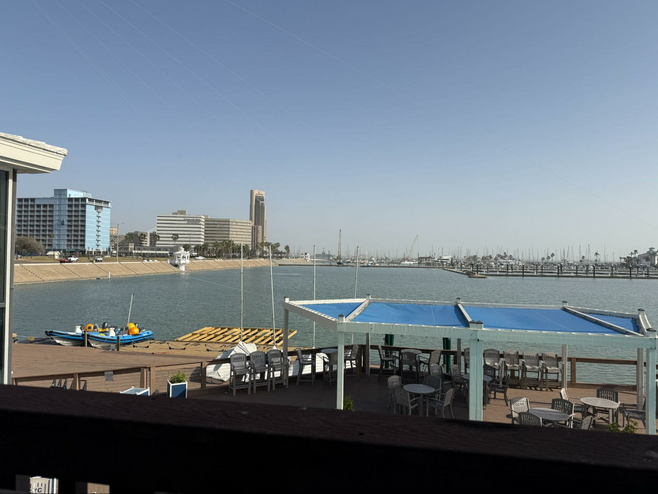View from the Corpus Christi Yacht Club of their patio and a portion of the bay behind, including some high-rise buildings on the waterfront.