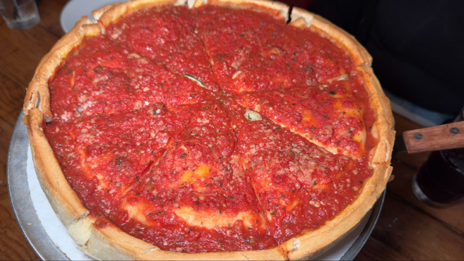A 15-inch pizza with red tomato sauce and thick crust on a metal dish with a knife.