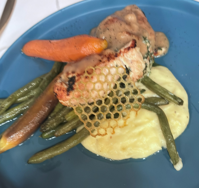 A chicken breast with gravy on a bed of mashed potatoes with carrots and green beans.