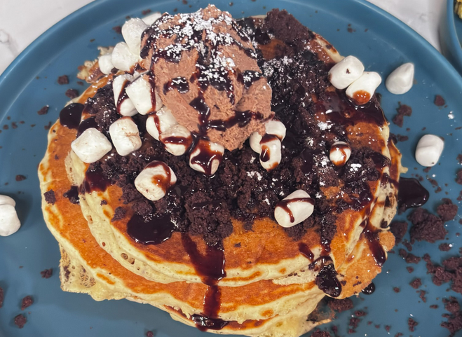 Campfire Chronicles pancakes are covered it chocolate sauce, marshmallows, and daRk chocolate sauce.