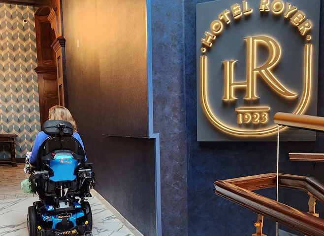 Marcia Frost is riding her wheelchair on a marble ramp next to a Hotel Royer sign.