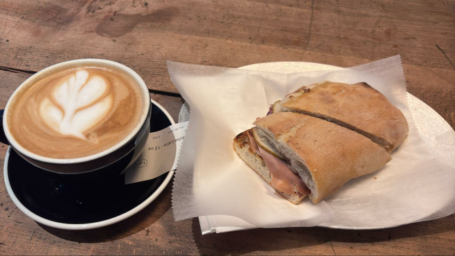 A pistachio latte in a large mug and a prosciutto and fig panini next to it as served at Tatte Bakery & Cafe in Boston near the Hyatt Regency.