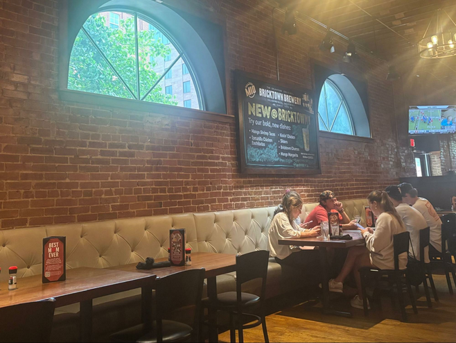 Diners at table with corner TV and large half windows in a brick wall