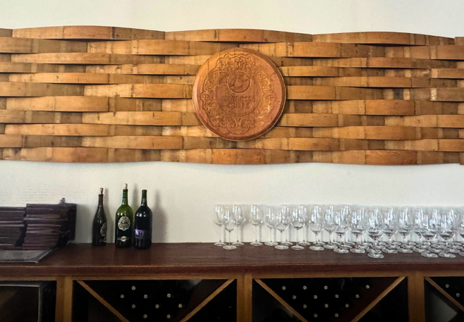 A cork logo of a wine company on the wall with wine bottles and glasses on a shelf.