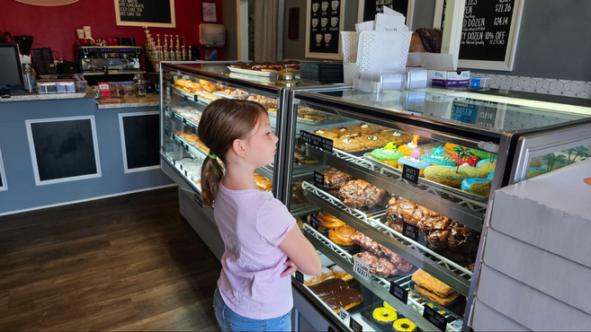 An 8-year-old standing in front of a display case of the donuts trying to decide which to choose. 