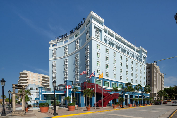 Blue multi-story hotel in Old San Juan with flags and trees next to a Walgreens.