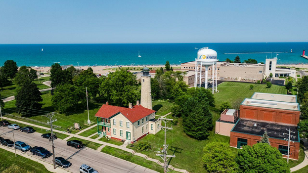 A quaint building in front of a lighthouse on a street. In the background is the ocean.
